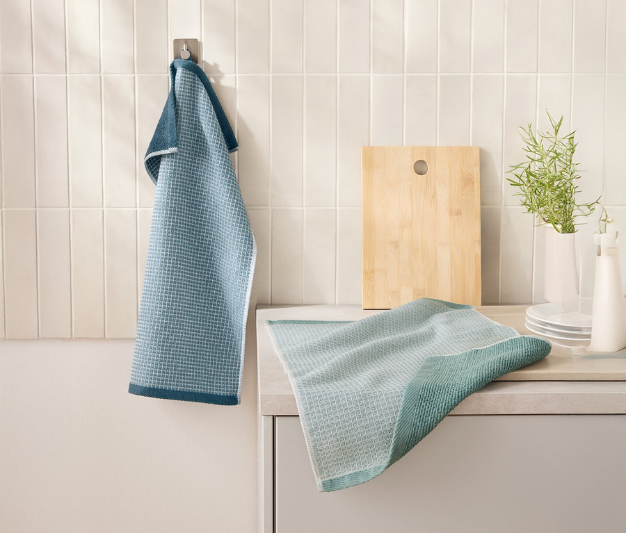 Un 2
Linges de cuisine à nids d’abeilles bleu est accroché à un crochet à côté d’une planche à découper. Un autre torchon est posé sur un comptoir de cuisine.