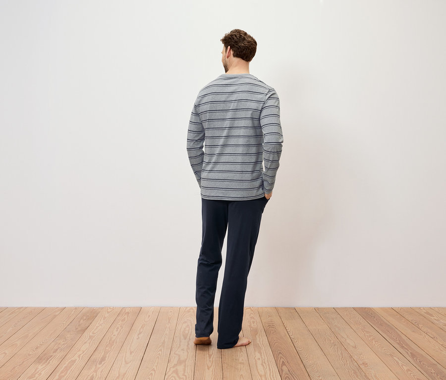 Un homme, dos à la caméra, porte un t-shirt à manches longues rayé et un pantalon bleu marine.