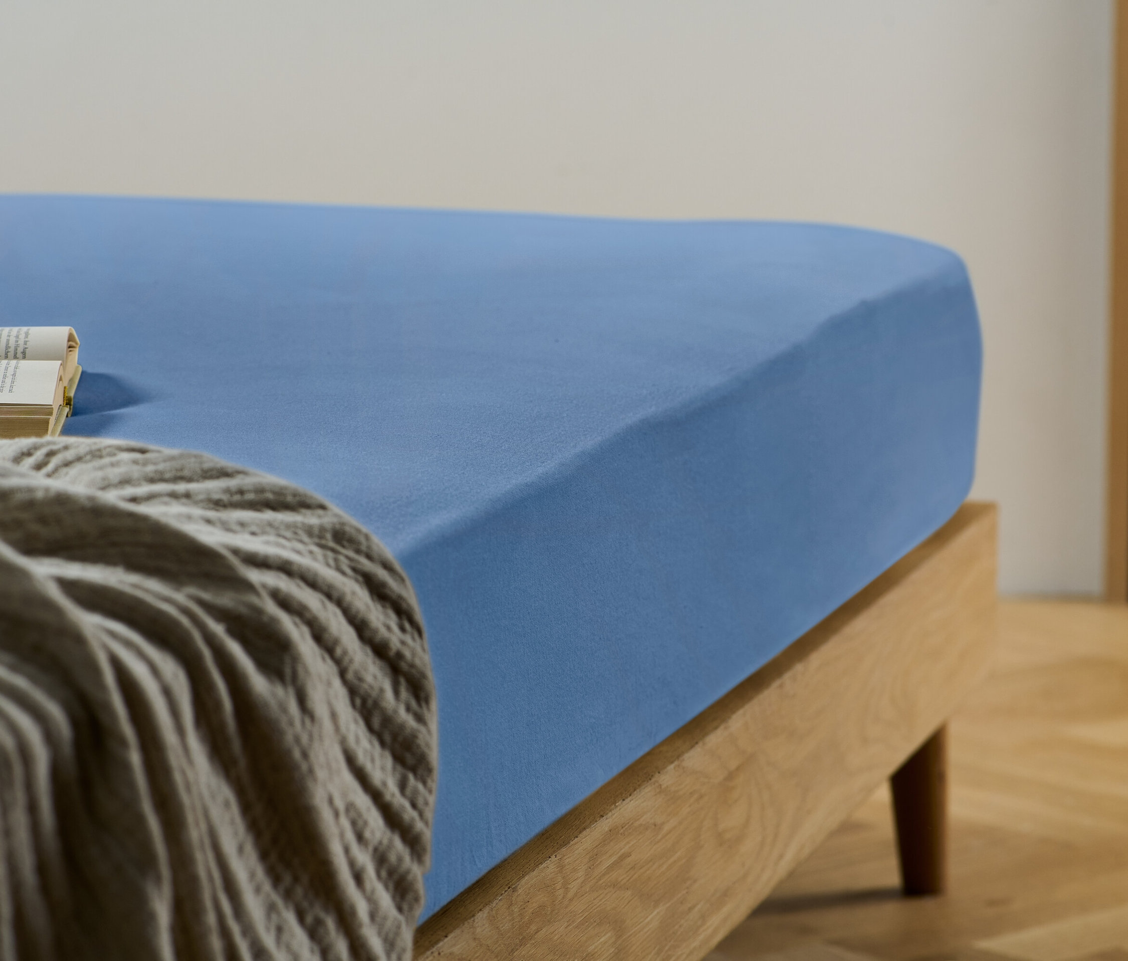 Gros plan d'un drap-housse bleu sur un lit avec un livre et une couverture grise.