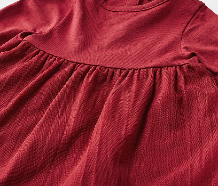 Gros plan sur une robe rouge à manches longues avec une jupe plissée.