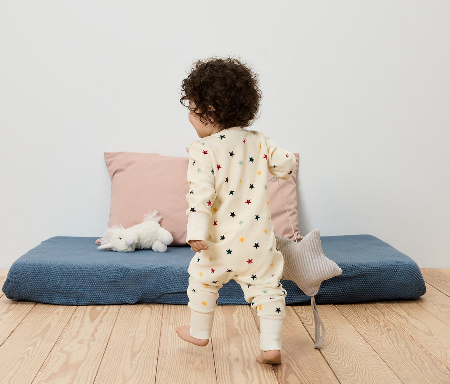 Un enfant en pyjama étoilé marche sur un plancher en bois à côté d'un coussin et d'un tapis bleu.