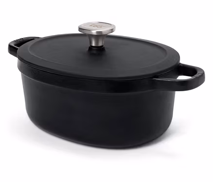 Cocotte ovale en fonte noire avec couvercle et poignée argentée sur fond blanc.