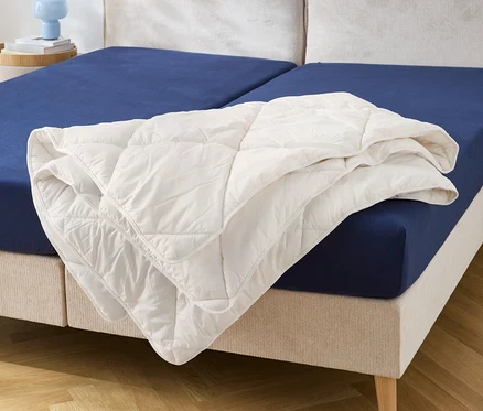 Sur un lit avec un drap-housse bleu se trouve une couette blanche.