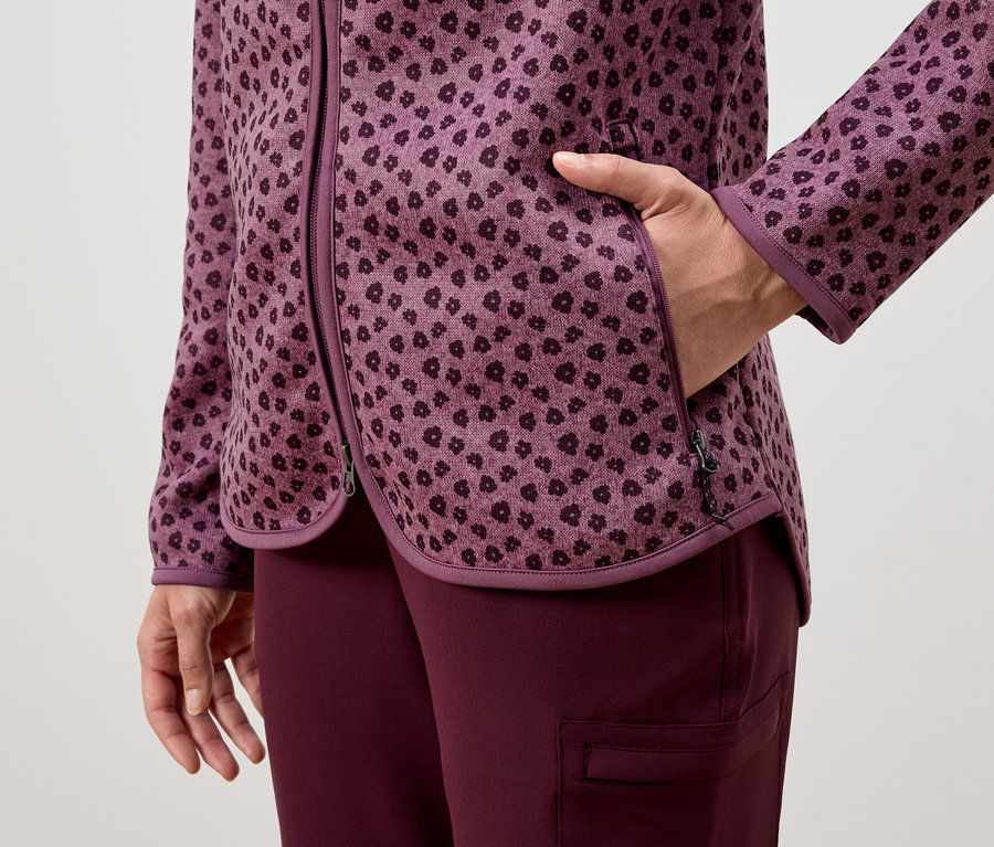 Une femme a la main dans la poche d'une veste violette à motifs, portée avec un pantalon violet.