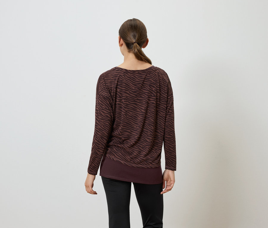Une femme, vue de dos, porte un T-shirt marron à manches longues et un pantalon noir.