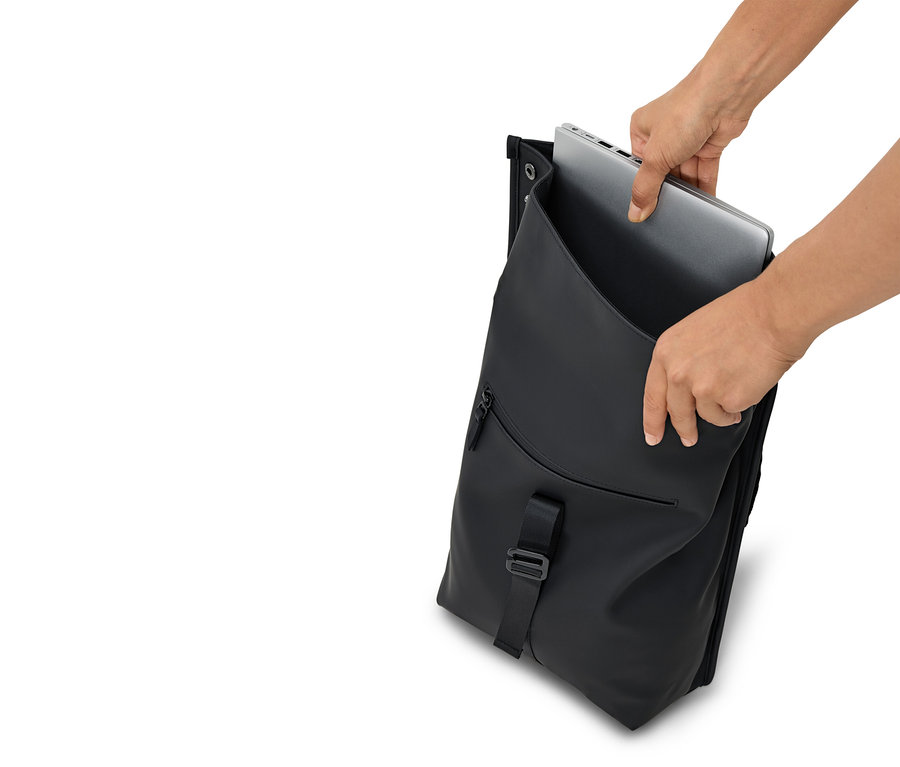 Des mains mettent un ordinateur portable argenté dans un sac à dos noir ouvert.