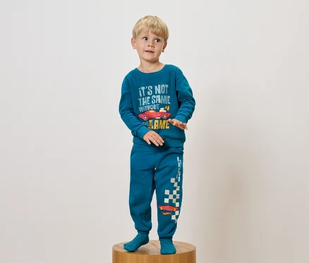 Garçon en pyjama bleu avec imprimé voiture debout sur un socle en bois.