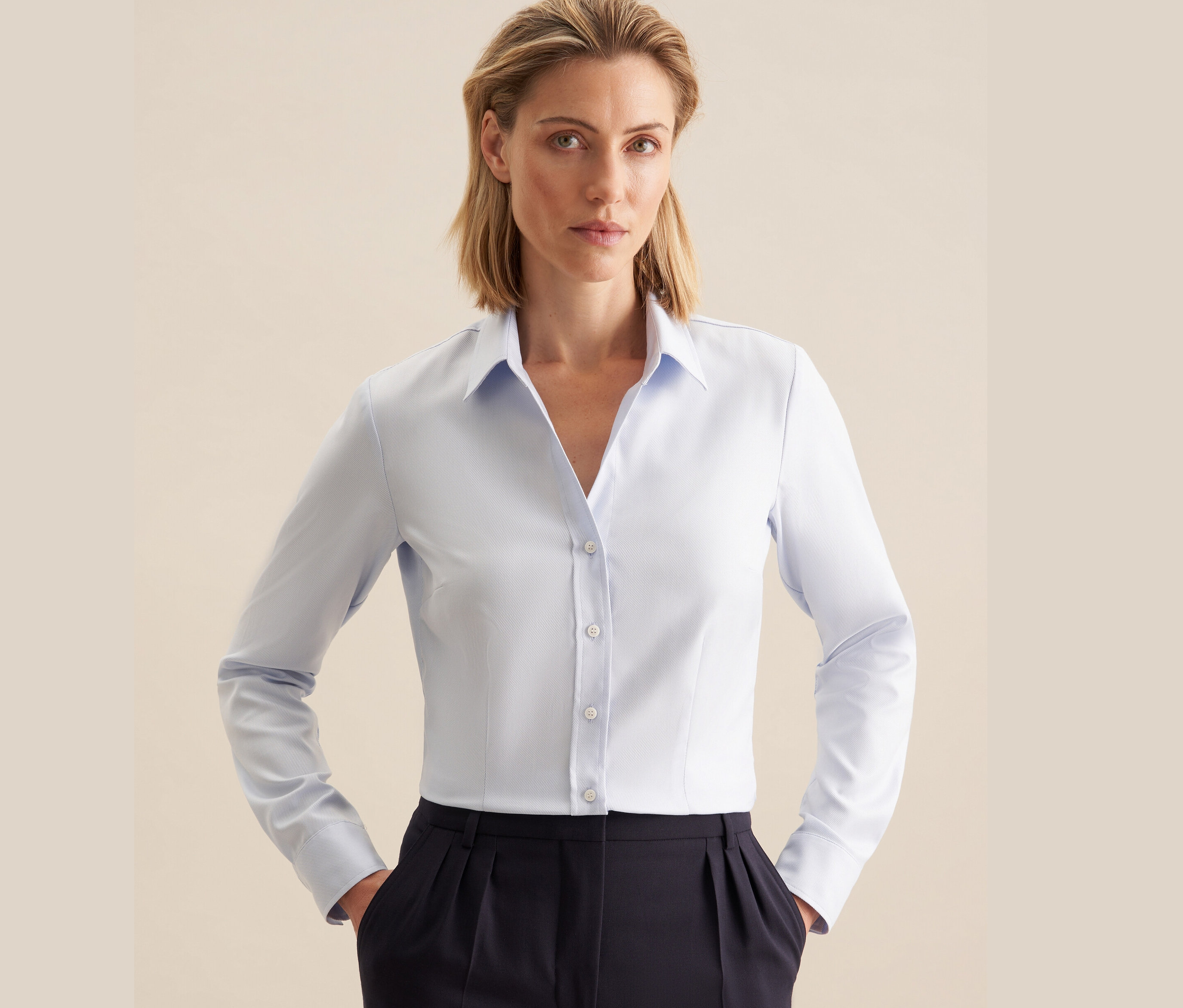 Une femme portant un chemisier en tulle Seidensticker bleu clair et un pantalon bleu foncé.