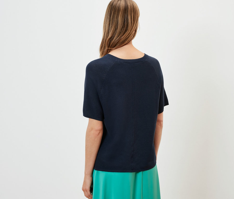 Vue arrière d'une femme portant un t-shirt en maille fine bleu marine et une jupe verte.