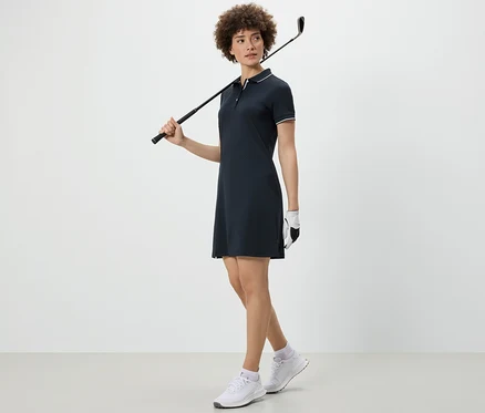 Femme tenant un club de golf sur l'épaule et portant une robe de sport.