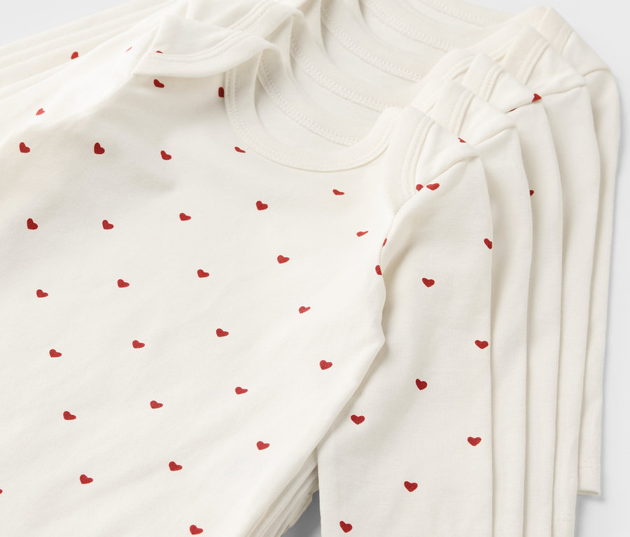 Pile de 5 bodys évolutifs pour bébé blancs avec un motif de coeurs rouges.