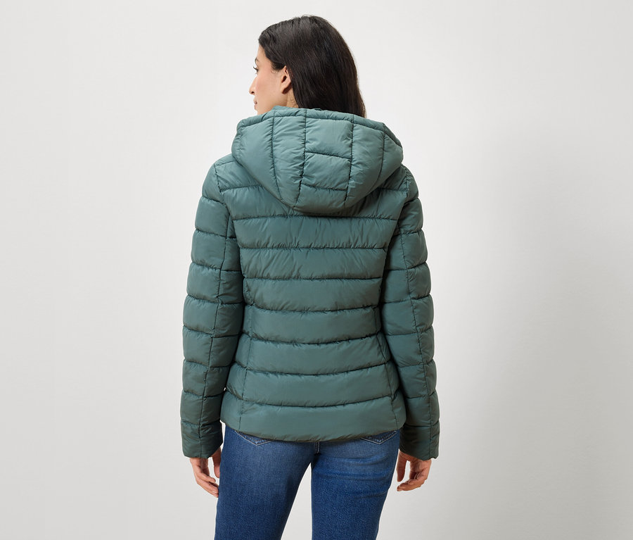 Une femme, le dos à la caméra, porte une doudoune verte et un jean.