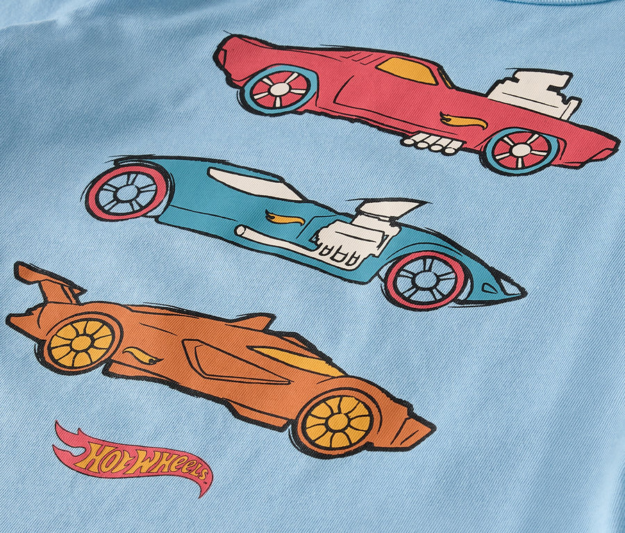 Sur un t-shirt bleu clair figurent trois voitures Hot Wheels dessinées en rouge, bleu et orange.