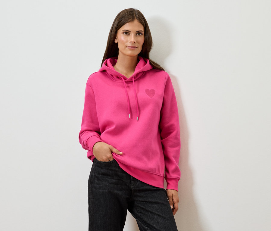 Femme portant un sweat à capuche rose et un jean noir.