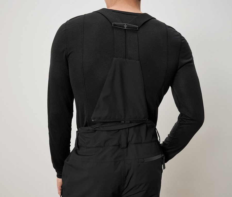 Vue arrière d'un homme portant des sous-vêtements thermiques noirs et un pantalon noir à bretelles.