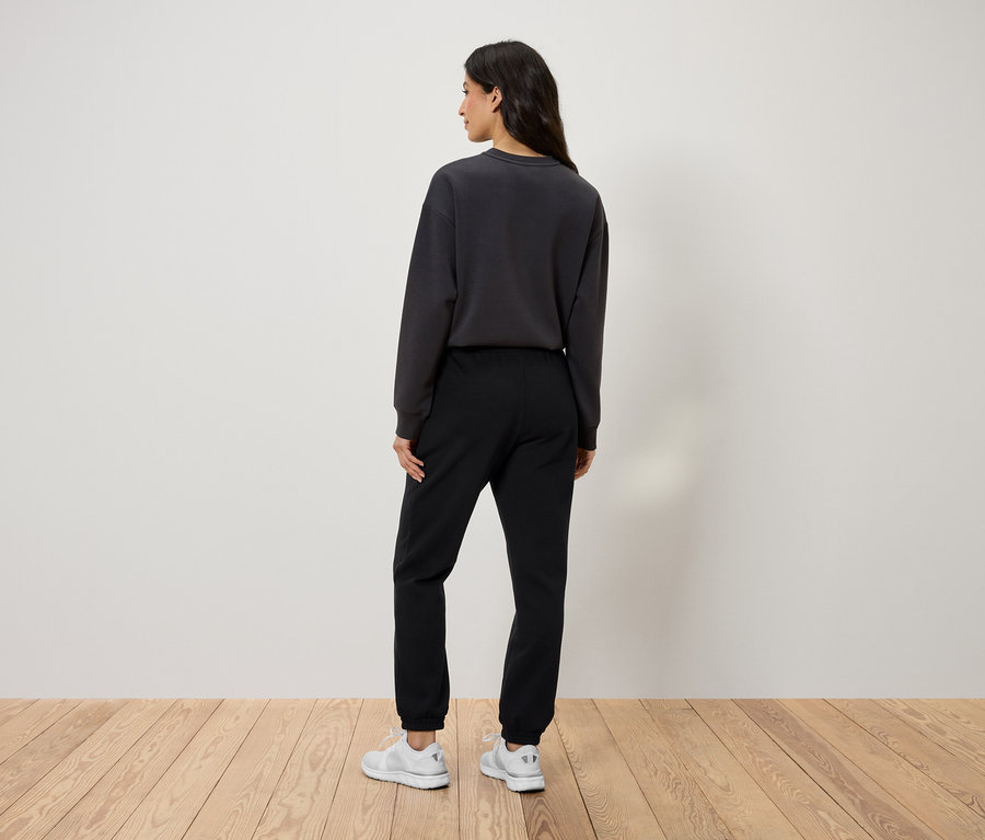 Vue arrière d'une femme portant un pantalon de survêtement noir, un sweat-shirt gris et des chaussures blanches.