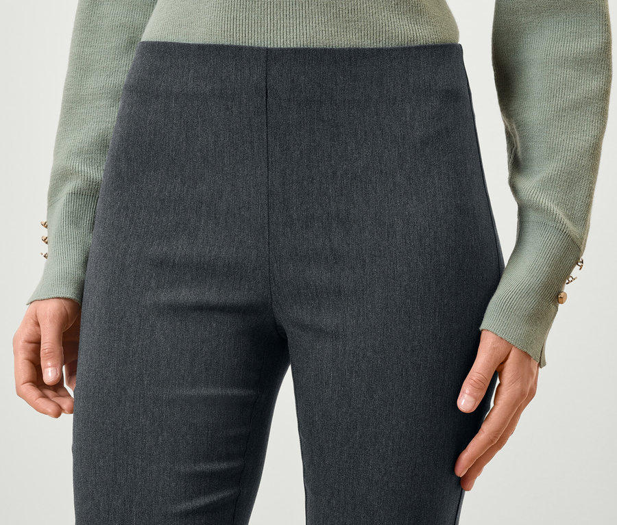 Détail d'une femme portant un pantalon gris et un pull vert clair.