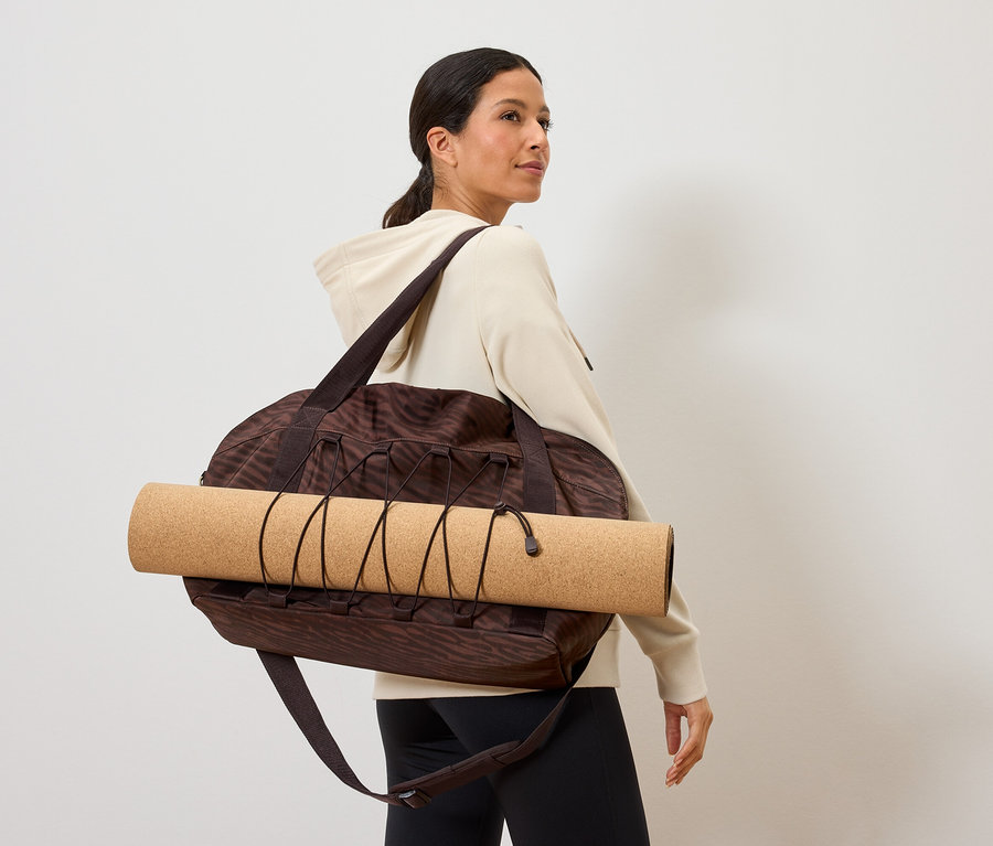 Femme portant un sac de sport marron à motifs avec un tapis de yoga dessus