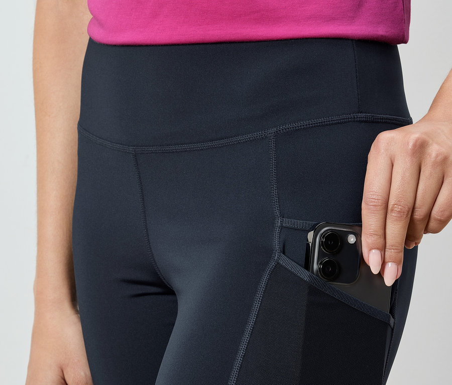Femme glissant un smartphone dans la poche d'un legging bleu marine.