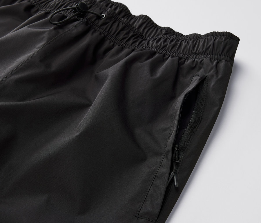 Gros plan sur un pantalon de pluie high-tech noir avec une taille élastique et une poche zippée.