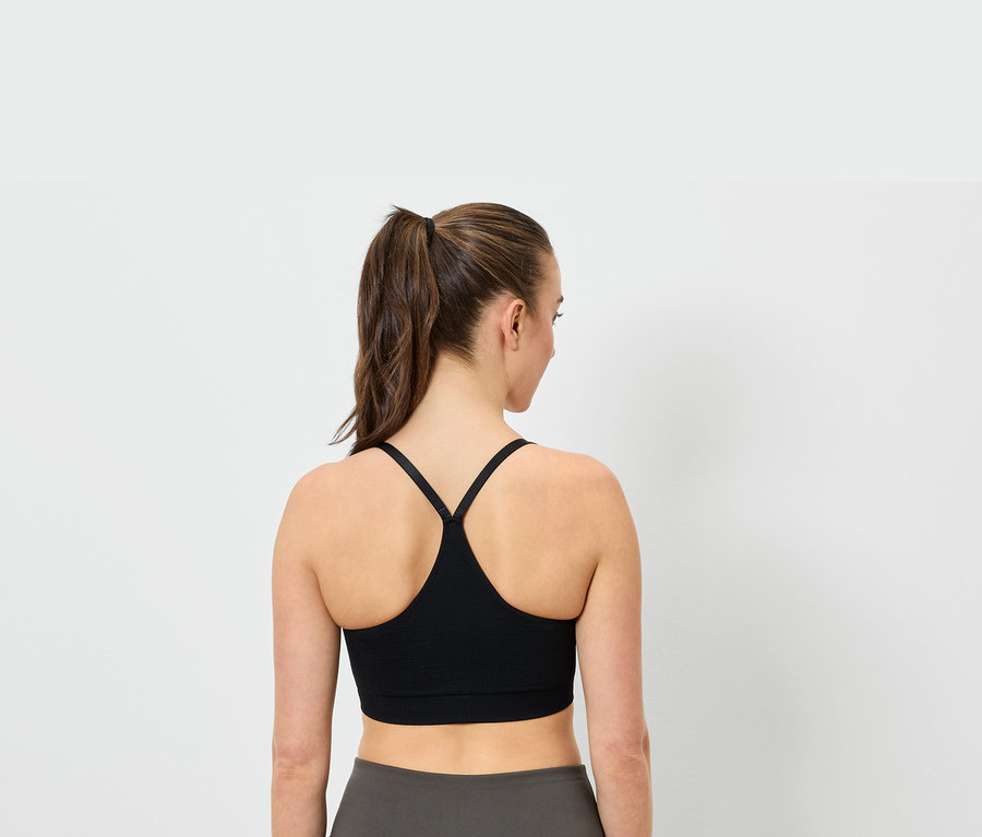 Vue arrière d'une femme avec une queue de cheval portant un soutien-gorge de sport noir et un legging gris.