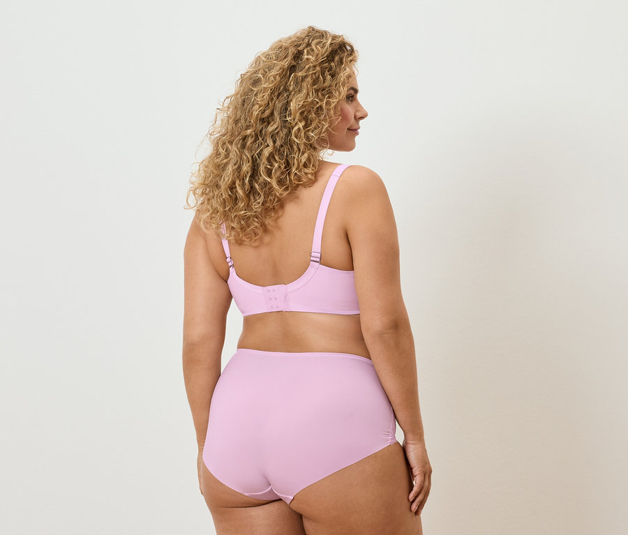 Une femme aux cheveux bouclés se tient dos à la caméra et porte un soutien-gorge et une culotte lilas clair.