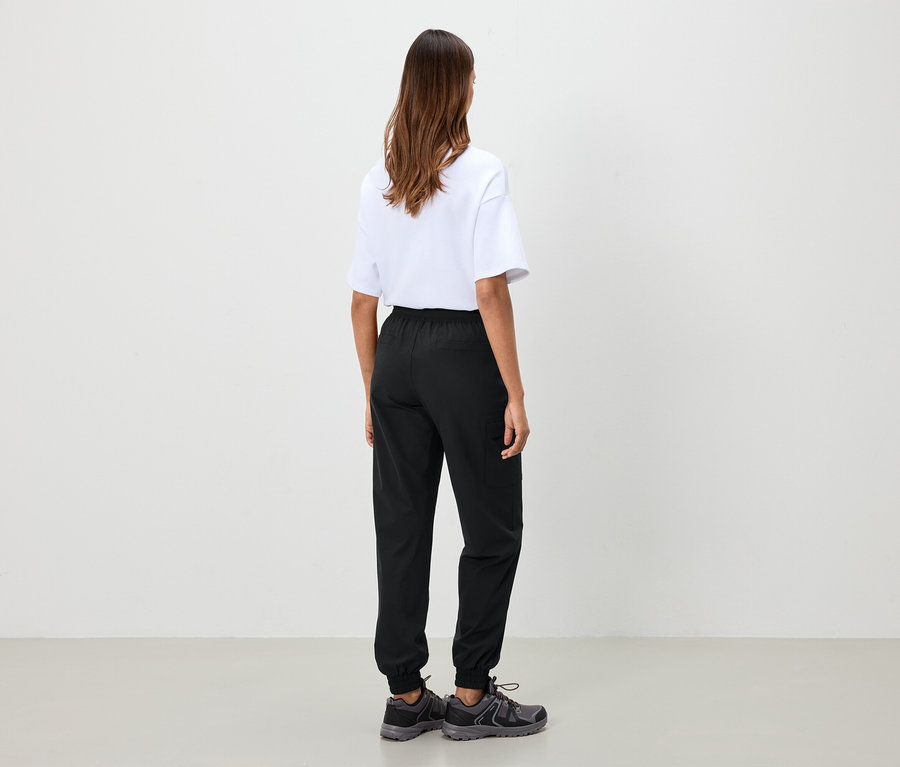 Une femme, vue de dos, porte un t-shirt blanc, un pantalon noir et des chaussures grises.