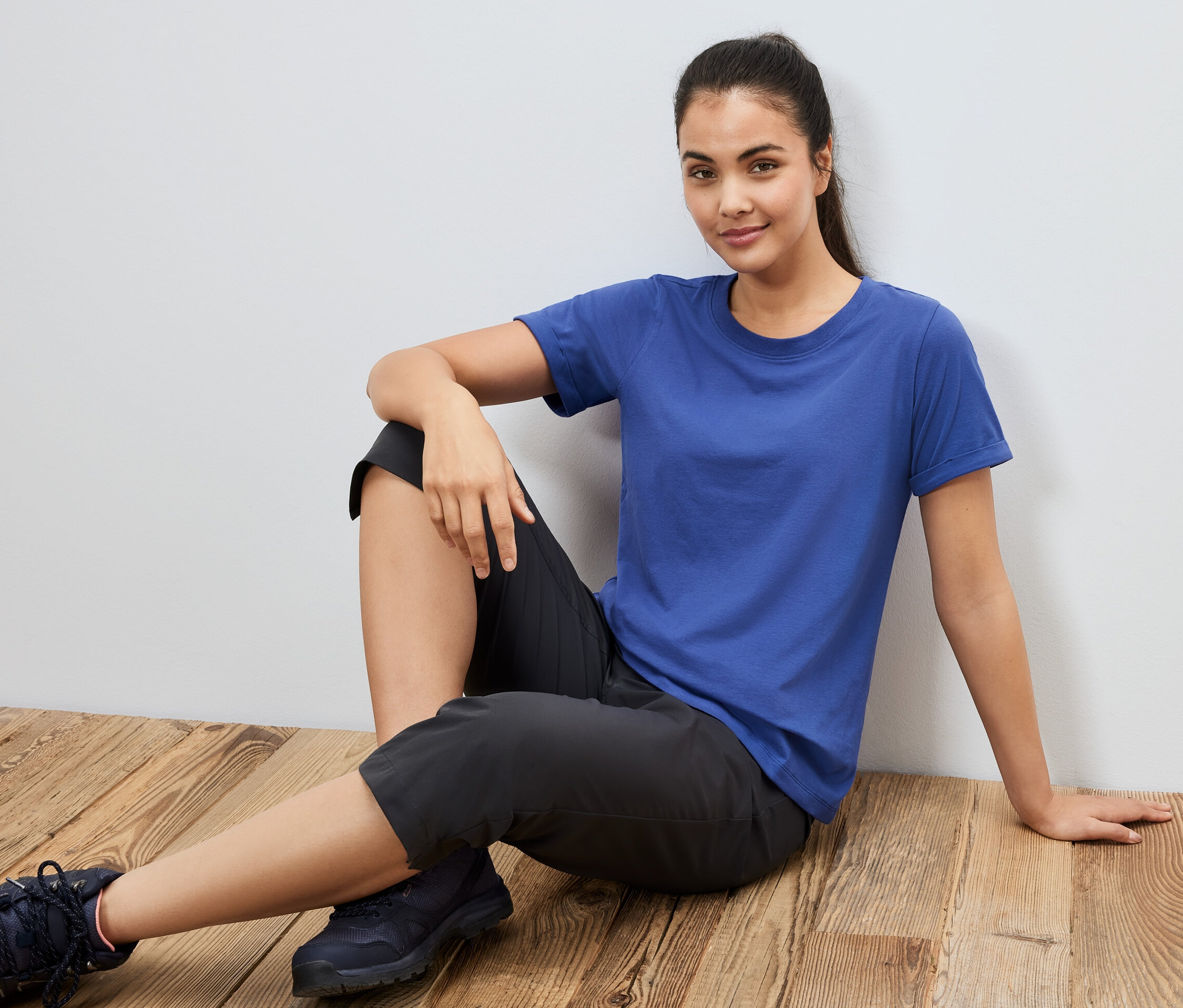 Une femme est assise par terre et porte un t-shirt de sport bleu.