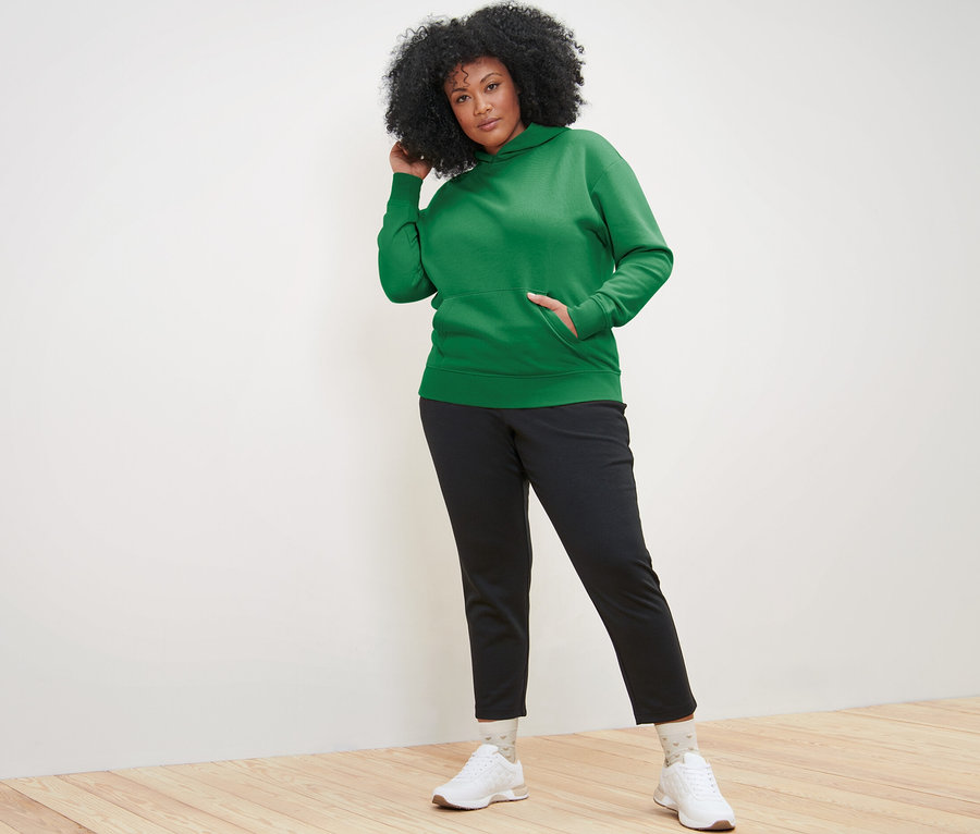 Femme posant dans un sweat à capuche vert et un pantalon noir.