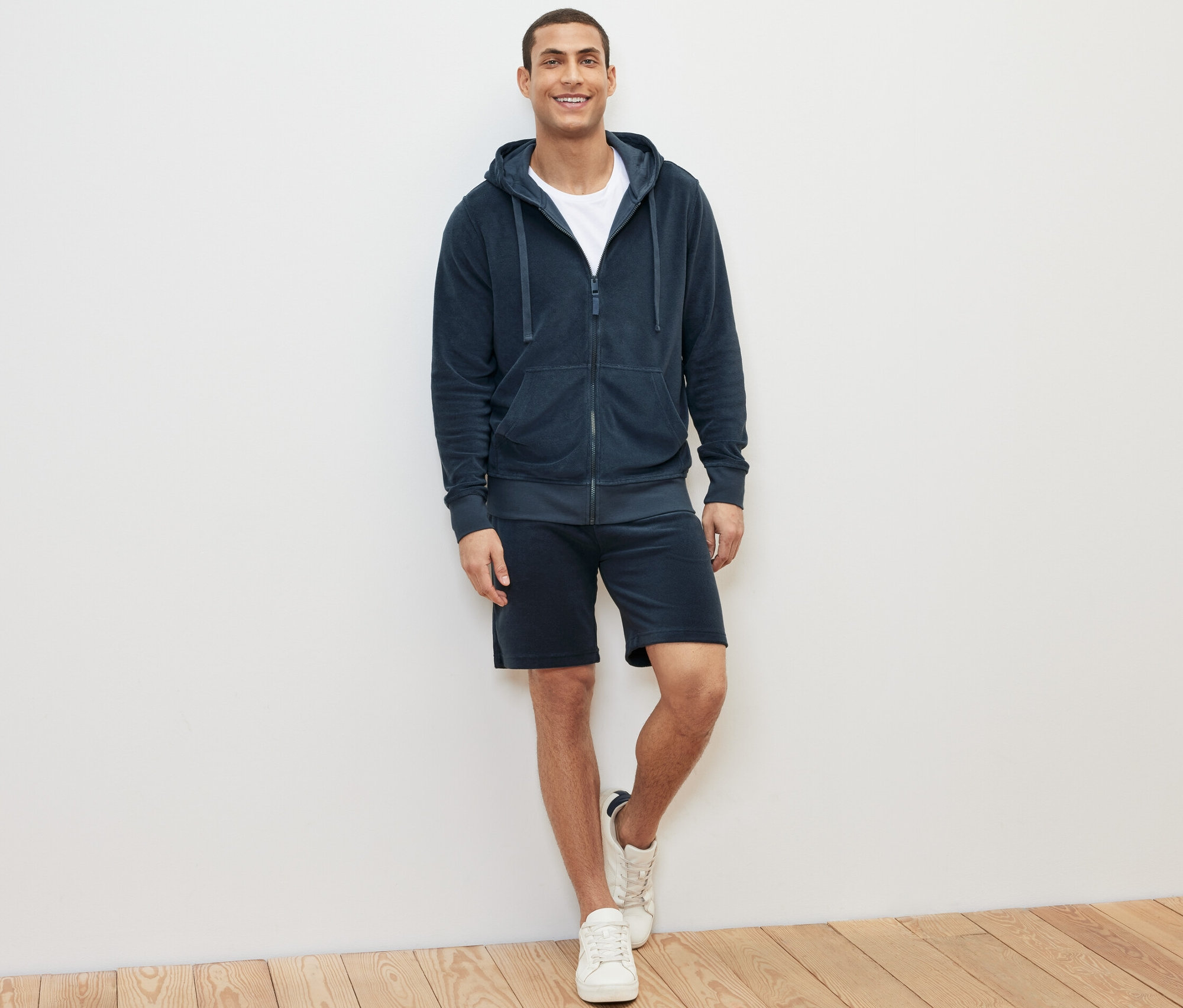 Un homme debout portant un sweat-shirt à capuche en tissu éponge bleu, un t-shirt et un short.