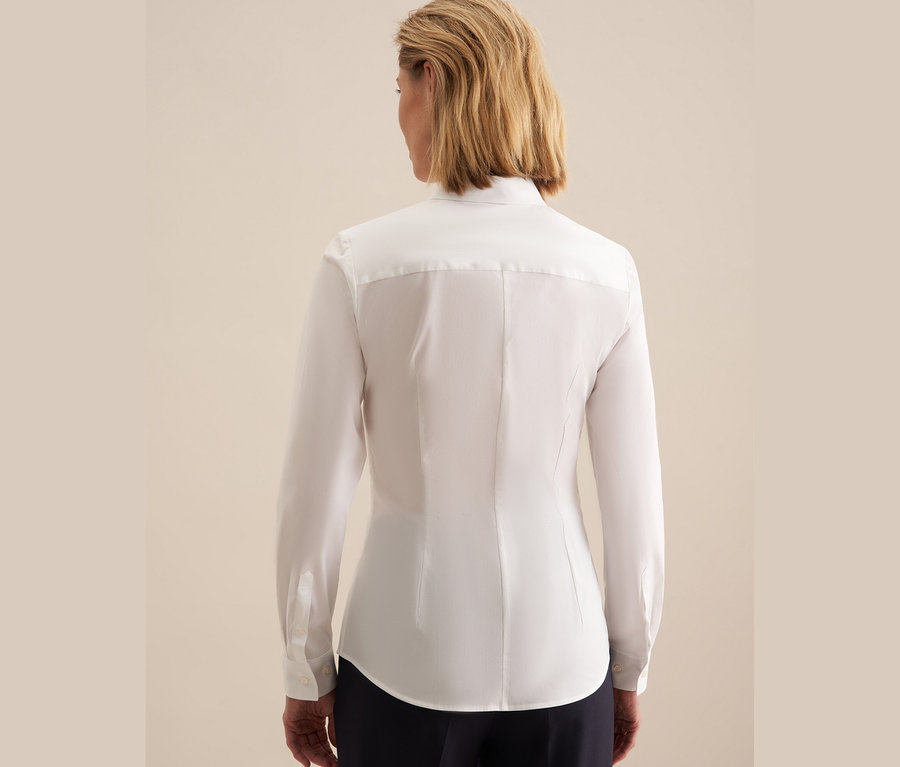 Vue arrière d'une femme aux cheveux blonds courts portant un chemisier Seidensticker Slimfit blanc et un pantalon bleu marine.