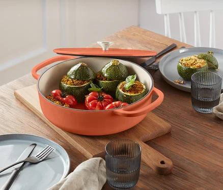 Courgettes farcies et tomates dans une casserole orange sur une planche à découper en bois.