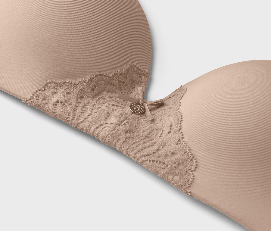 Gros plan d'un soutien-gorge couleur chair avec des finitions en dentelle et un petit bouton décoratif.