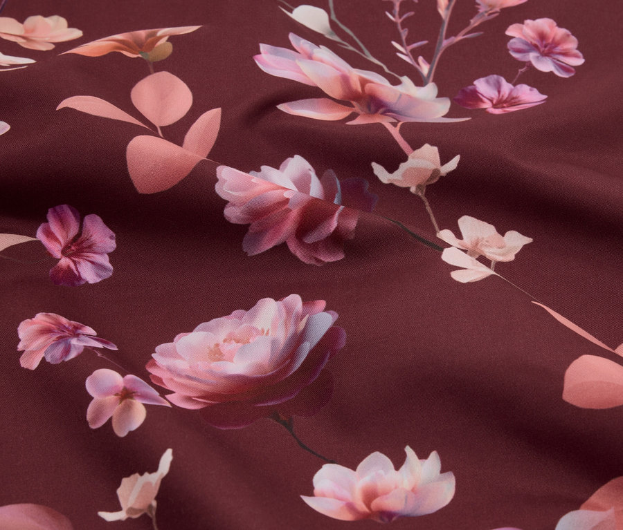 Gros plan d'un tissu avec un motif de roses roses et de feuilles sur un fond bordeaux.