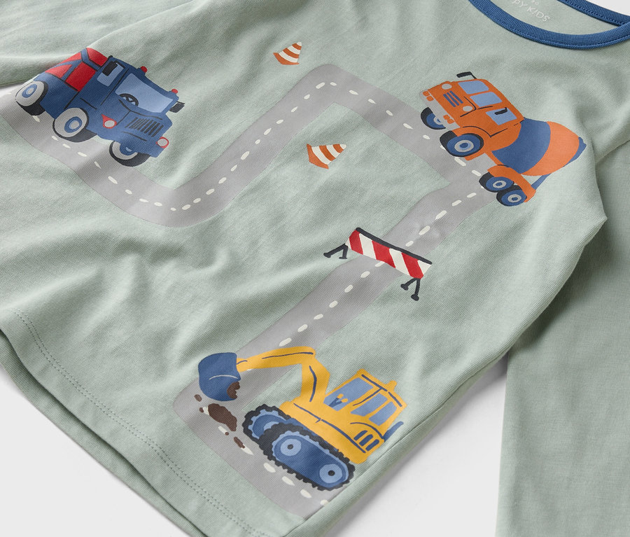 Sur une chemise vert clair figurent des illustrations de véhicules de construction sur une route grise.