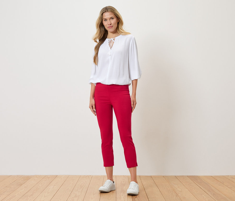 Une femme se tient debout et porte un chemisier blanc, un pantalon rouge et des baskets blanches.