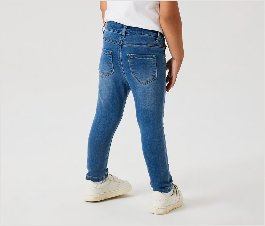 Enfant vu de dos portant un jegging pour enfant NAME IT et des chaussures blanches.
