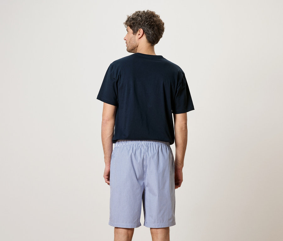 Un homme vu de dos, portant un t-shirt bleu marine et un short rayé bleu et blanc.