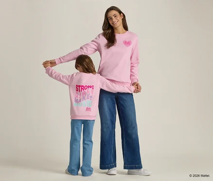 Une femme et un enfant se tiennent la main, tous deux portant des pulls roses assortis et des jeans.
