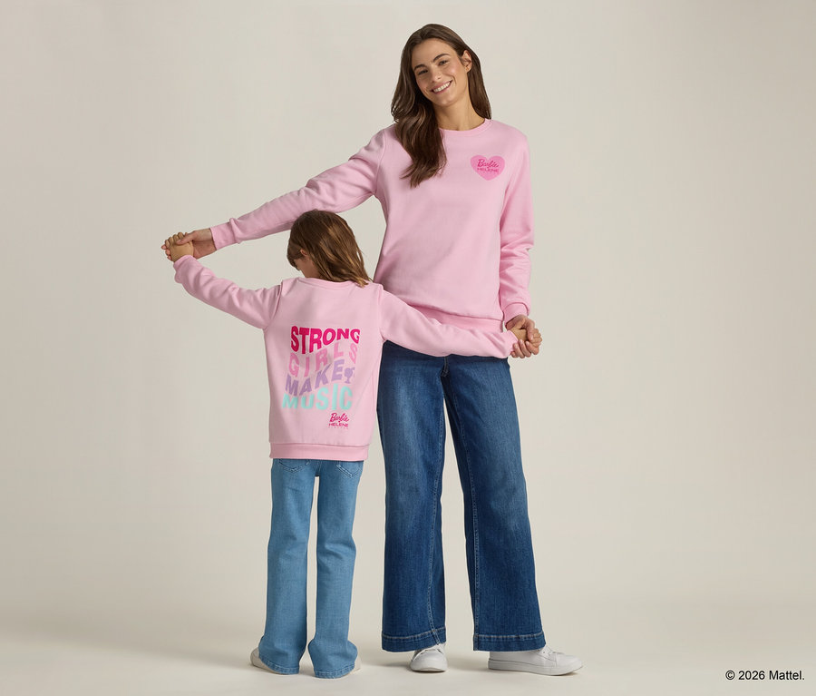 Une femme et un enfant se tiennent la main, tous deux portant des pulls roses assortis et des jeans.