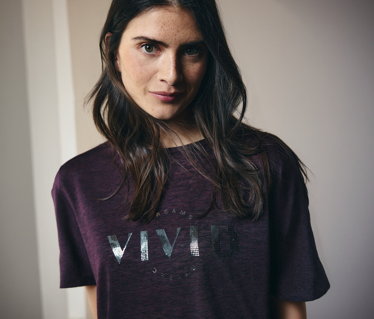 Une femme aux longs cheveux bruns porte un t-shirt marron avec l'inscription "Vivid Dreams".