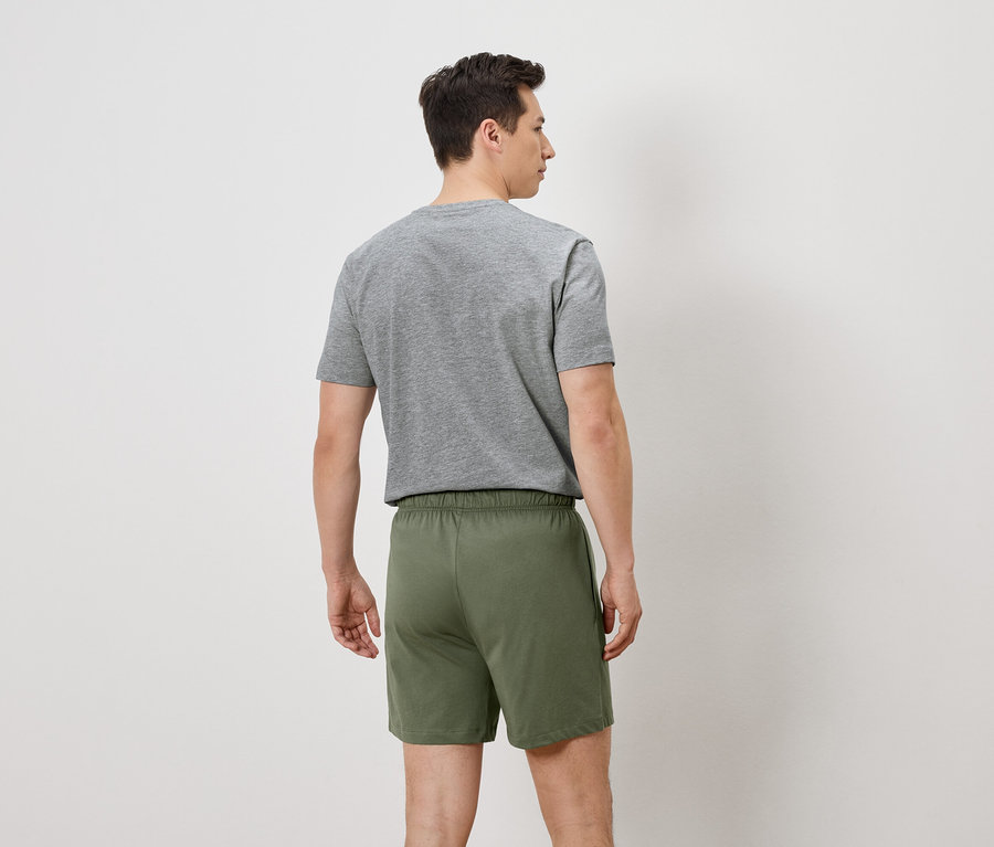 Vue arrière d'un homme portant un t-shirt gris et un short vert sur fond blanc.