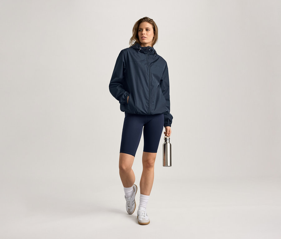 Femme portant une veste de pluie, un cycliste et une gourde. Elle porte des chaussettes et des baskets.