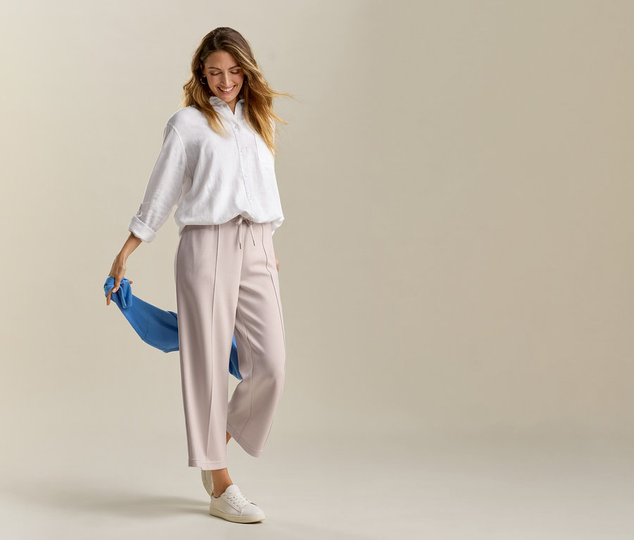 Femme portant un pantalon beige et une blouse longue en lin blanche tenant un tissu bleu.