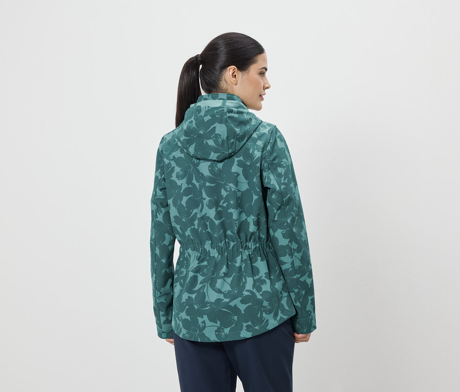 Femme vue de dos, avec une queue de cheval, porte une veste verte à fleurs avec capuche et cordon de serrage.
