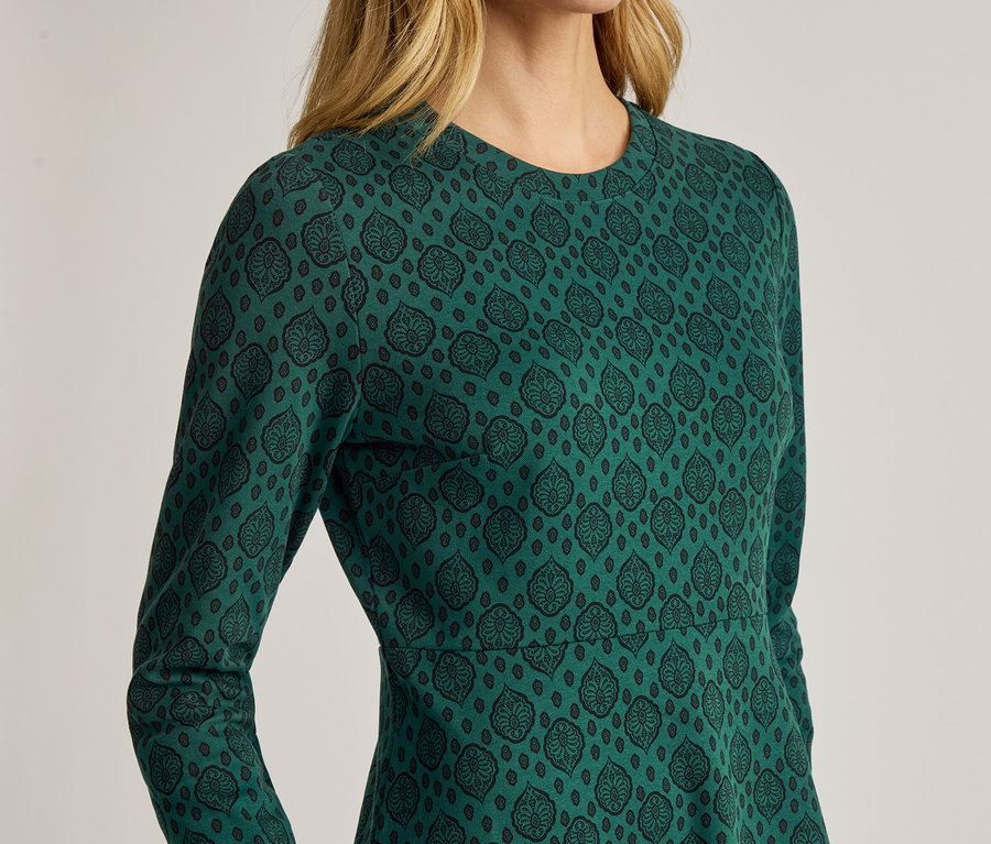 Une femme porte une robe verte à manches longues avec un motif noir.