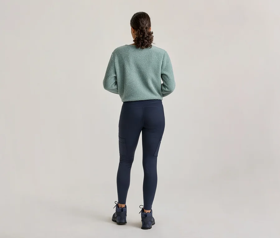 Une personne vue de dos, portant un pull duveteux vert clair, un legging bleu foncé avec des poches latérales et des chaussures de randonnée bleu foncé.