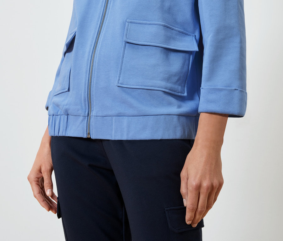 Une femme porte une veste bleu clair et un pantalon bleu foncé.