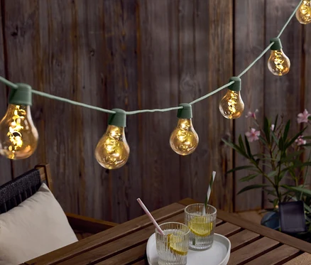 Guirlande lumineuse avec des ampoules suspendue au-dessus d'une table en bois avec des boissons et un chapeau.