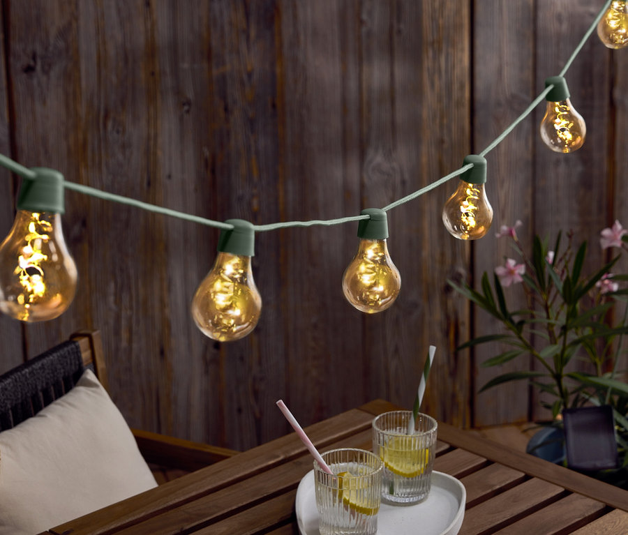 Guirlande lumineuse avec des ampoules suspendue au-dessus d'une table en bois avec des boissons et un chapeau.